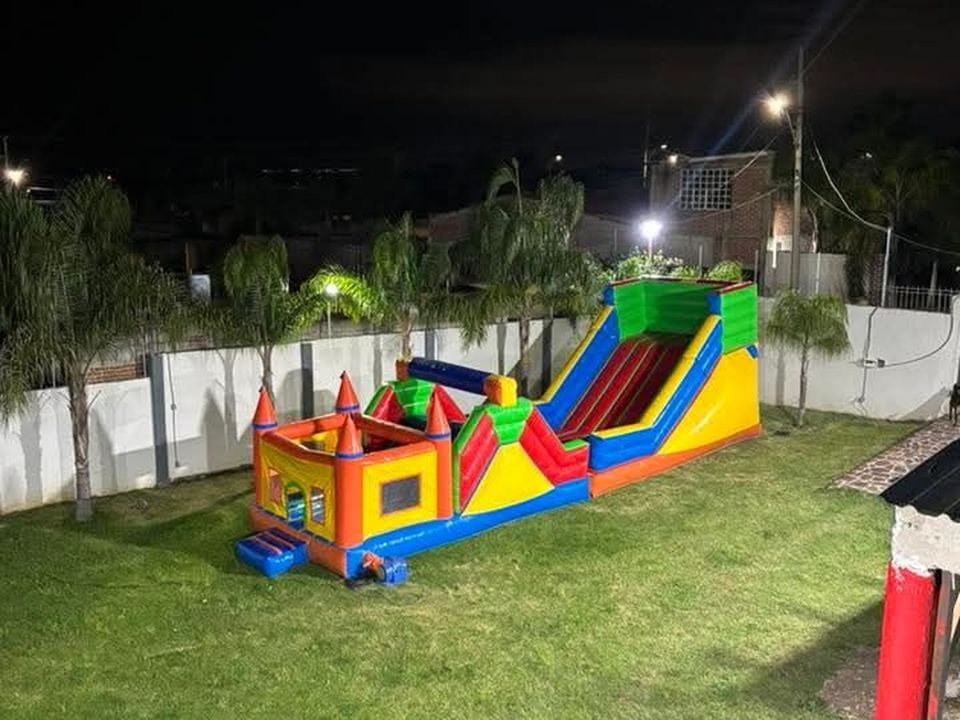 Castillo aventura inflable iluminado de noche, montado en un jardín con palmeras.