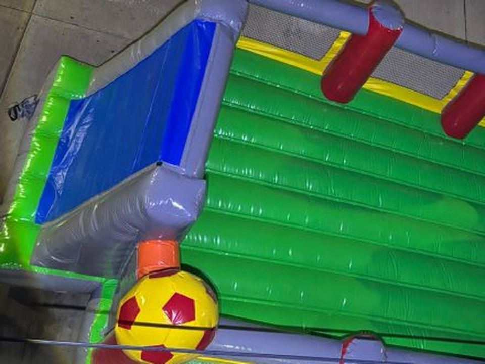 Cancha de fútbol inflable con pasto verde, porterías y balones grandes en las esquinas