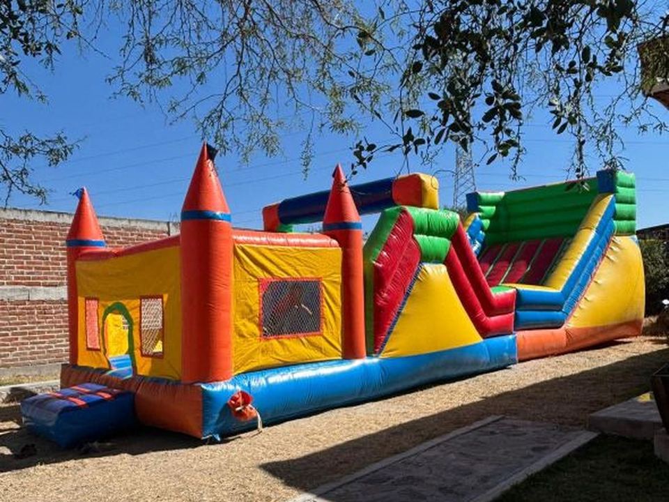 Castillo aventura inflable con torres, brincolín y resbaladilla lateral, montado en jardín de día